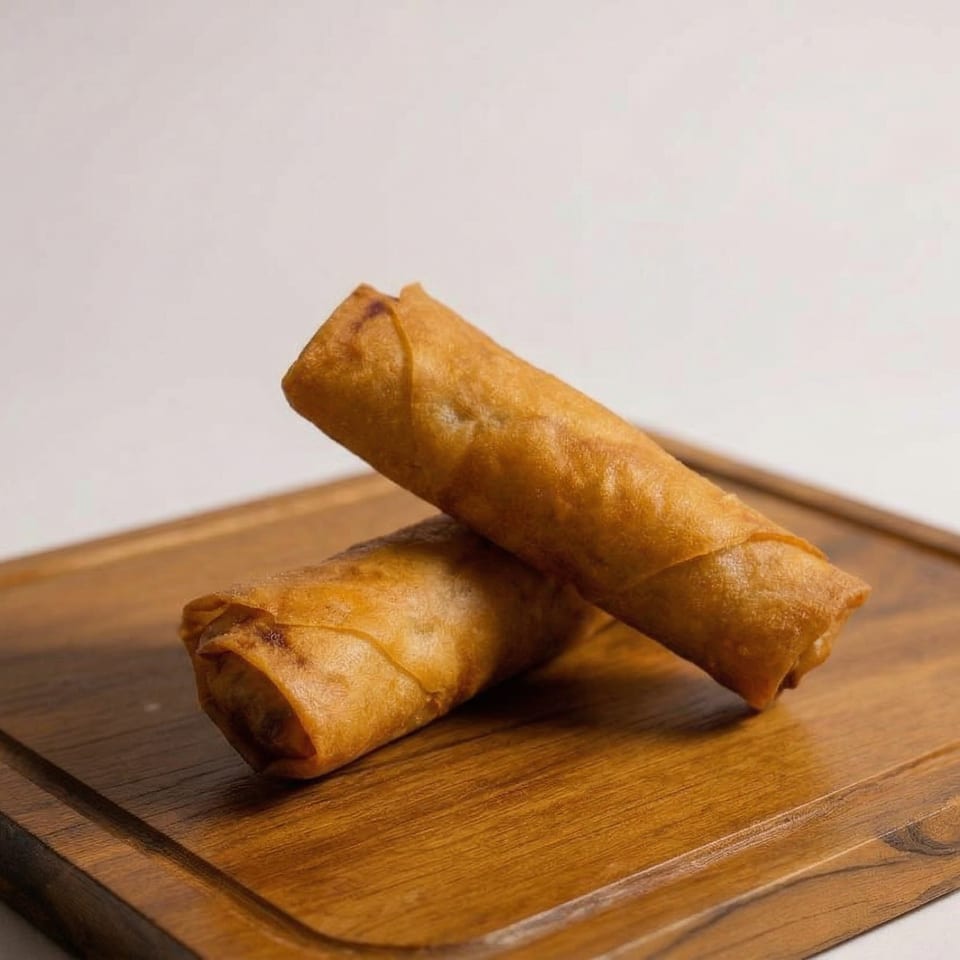 Two crispy, golden-brown spring rolls are arranged on a wooden cutting board against a white background.