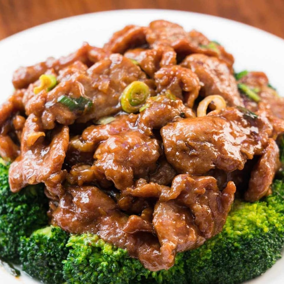 Close-up of beef and broccoli dish with a rich brown sauce and green onions on a white plate.