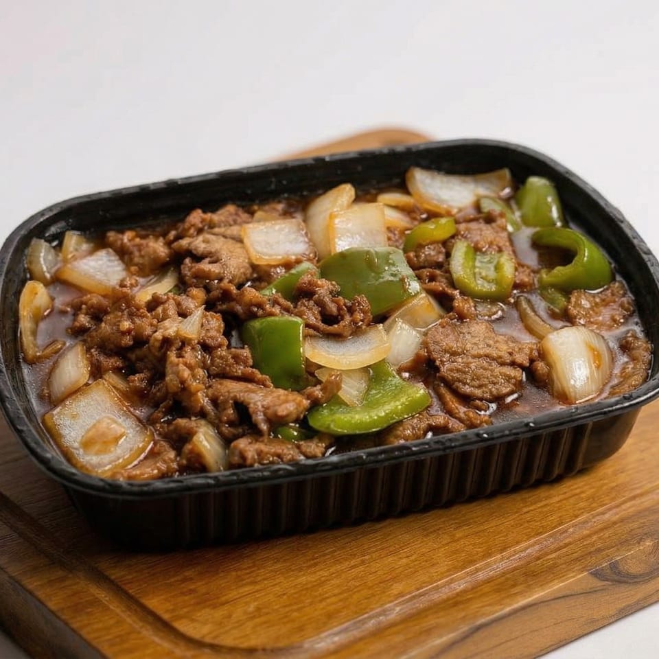 Beef and broccoli with onions and green peppers in a black container on a wooden board.